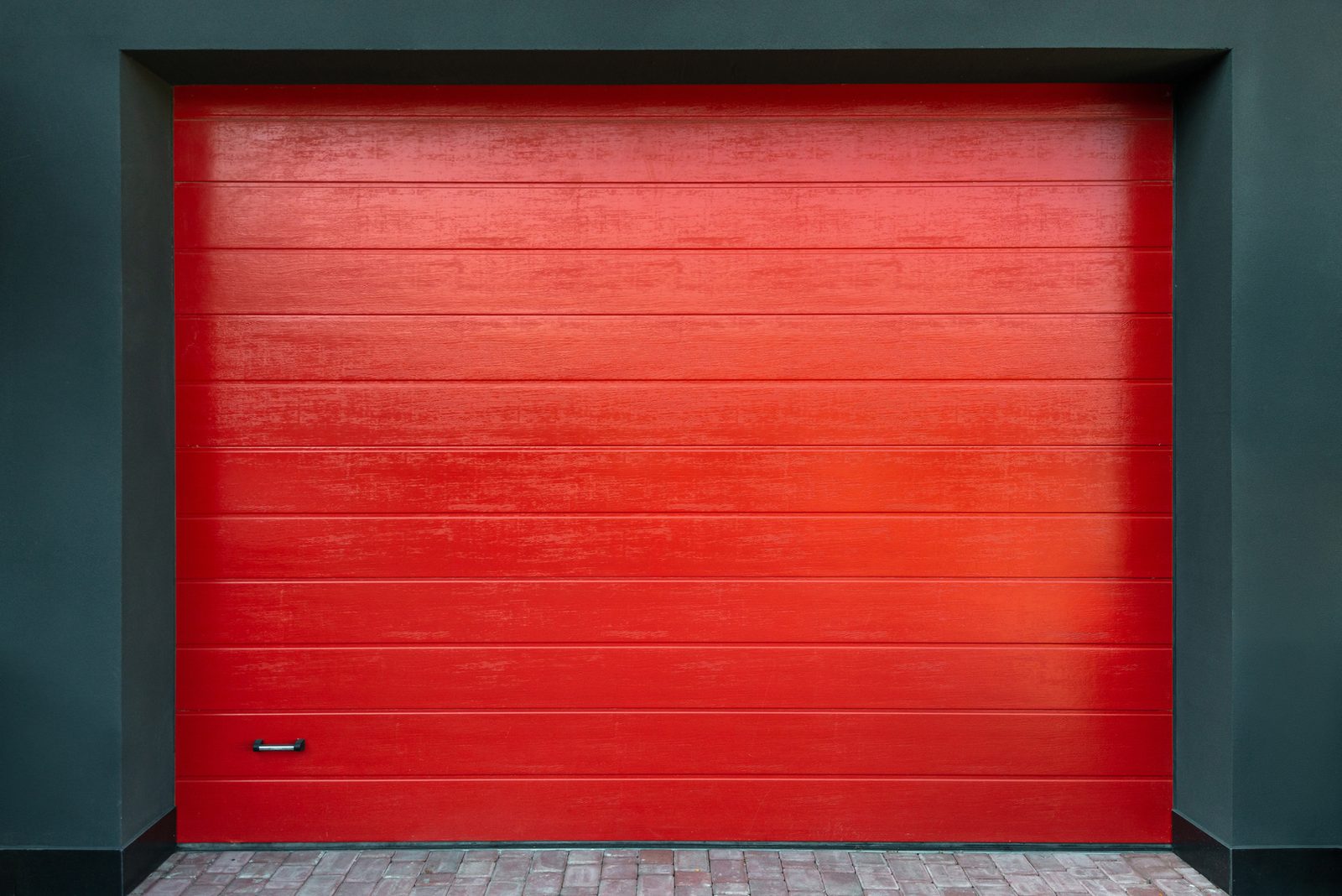 Bright red horizontal-panel garage door set in a dark wall